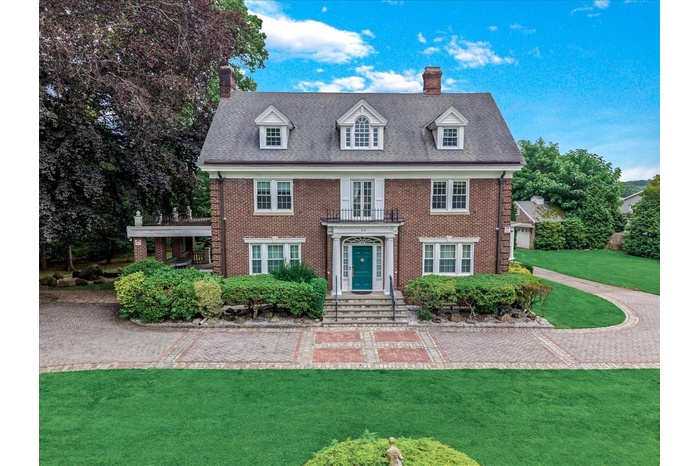 Georgian-style home featuring a chimney, a front yard, brick siding, and a balcony