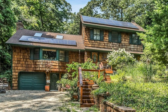 View of front of house with a chimney, a garage, roof with shingles, solar panels, and gravel driveway