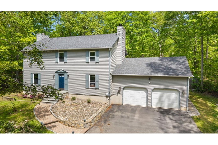 Colonial-style house featuring a chimney, a garage, driveway, a shingled roof, and view of wooded area