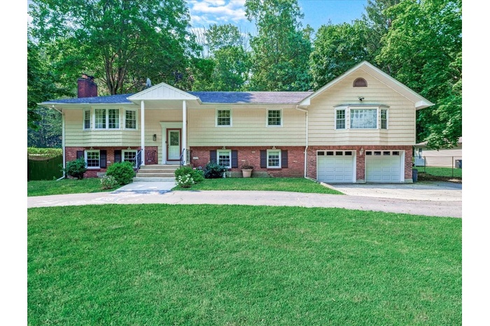 Bi-level home featuring concrete driveway, a garage, a front yard, a chimney, and brick siding