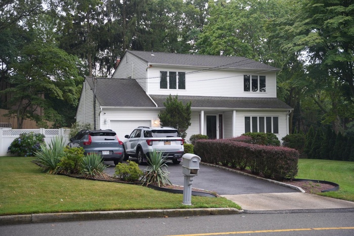 Traditional home with a garage, asphalt driveway, view of wooded area, and a shingled roof
