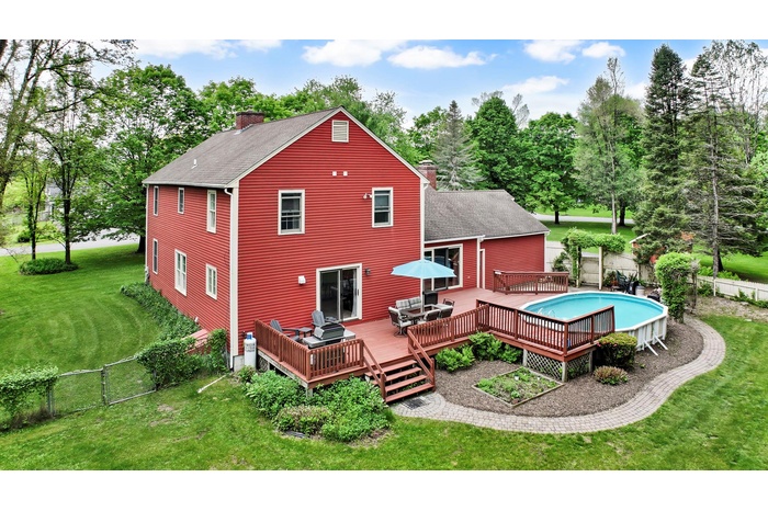 Rear view of property featuring a chimney, a shingled roof, a deck, and view of wooded area