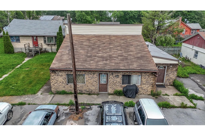 View of front of home with brick siding, uncovered parking, solar panels, and a shingled roof