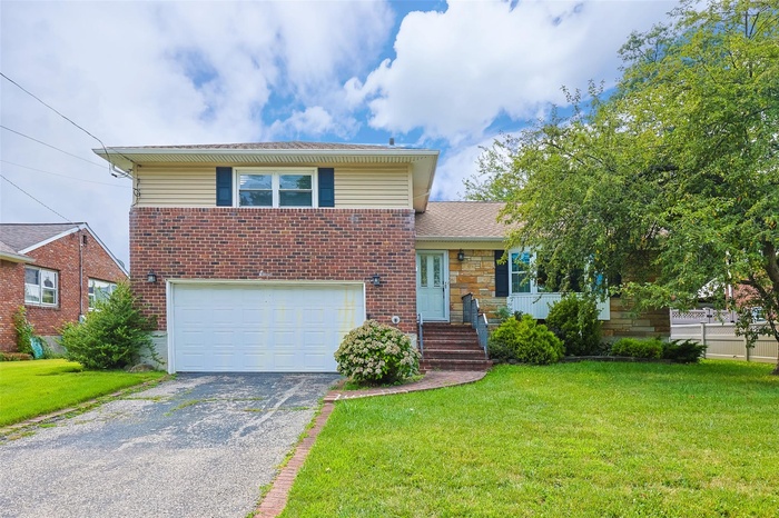 Split level home featuring a garage, a front lawn, asphalt driveway, and brick siding