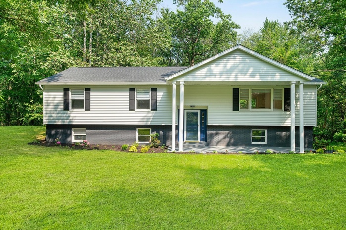 Bi-level home with a front lawn and view of wooded area