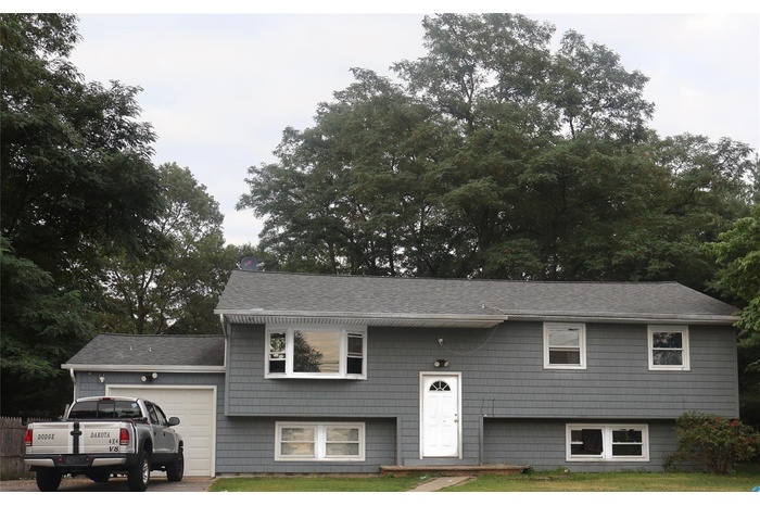 Split foyer home featuring a garage, a shingled roof, and a front lawn