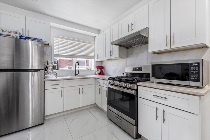 Kitchen featuring stainless steel appliances, under cabinet range hood, a sink, white cabinets, and recessed lighting