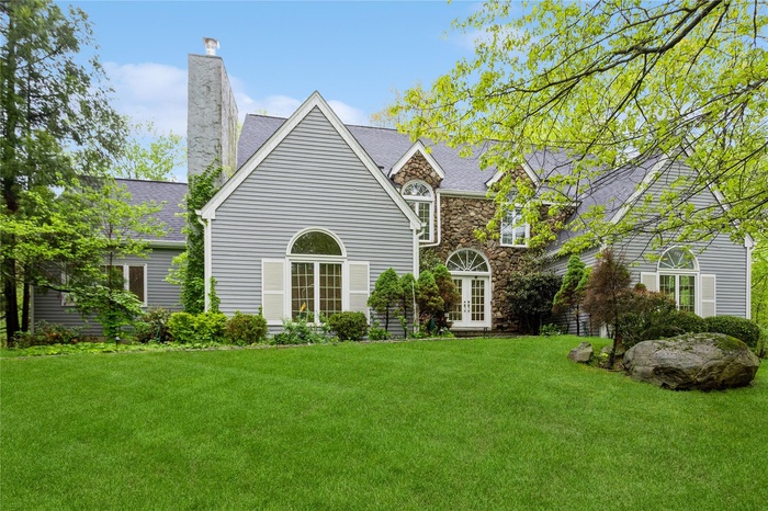 Rear view of house featuring french doors, a lawn, a chimney, and stone siding