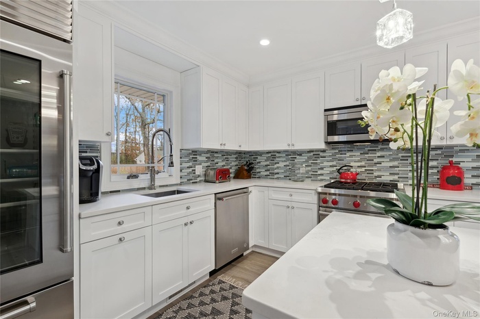 Kitchen with appliances with stainless steel finishes, light countertops, white cabinetry, backsplash, and recessed lighting