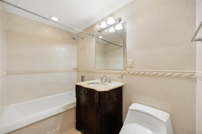 Bathroom with toilet, tile walls, vanity, and shower / washtub combination