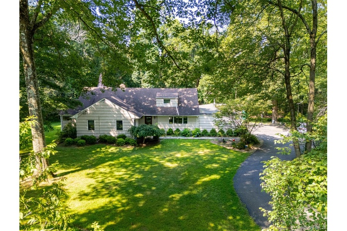 View of front of house featuring a front yard, view of scattered trees, roof with shingles, and asphalt driveway