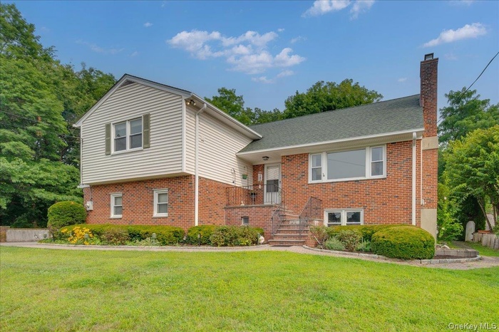 Front of home with brick siding, a chimney, and a front yard