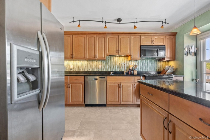 Kitchen featuring stainless steel appliances, backsplash, hanging light fixtures, brown cabinetry, and crown molding