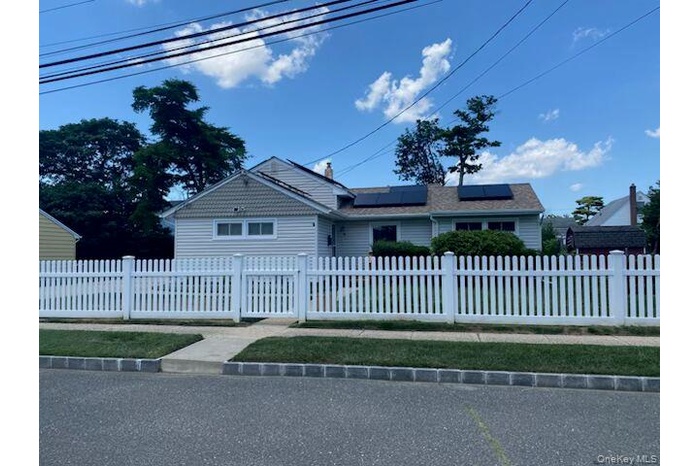 Single story home featuring roof mounted solar panels and a fenced front yard