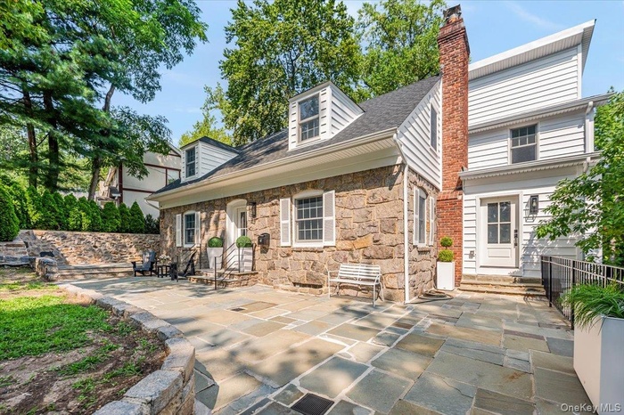 Back of house featuring entry steps, stone siding, a patio area, and a chimney