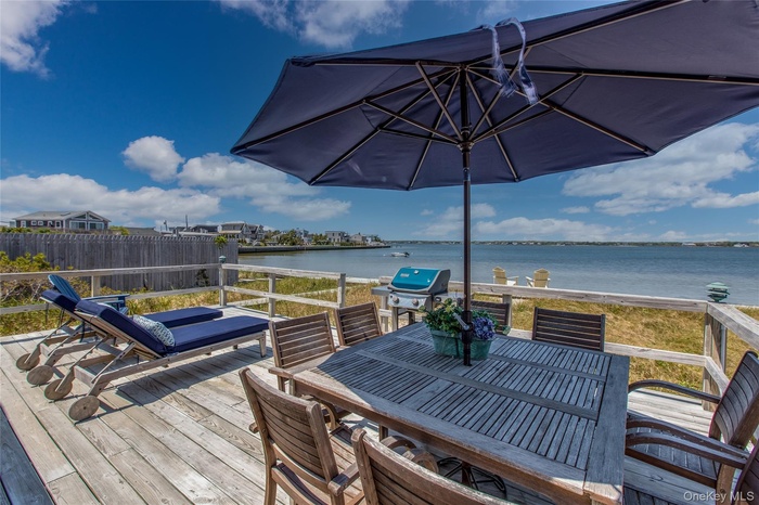 Wooden terrace with outdoor dining area, a water view, and a grill