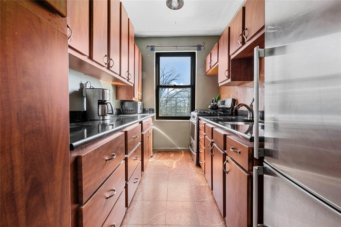 Kitchen featuring dark countertops, appliances with stainless steel finishes, a sink, backsplash, and light tile patterned floors