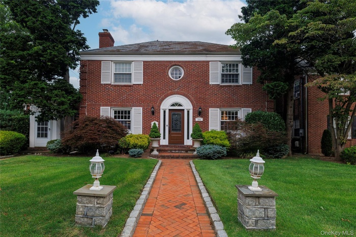 Colonial home with brick siding, a front yard, and a chimney