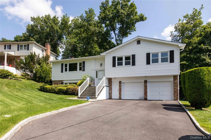Split foyer home with brick siding, a garage, asphalt driveway, and a front yard