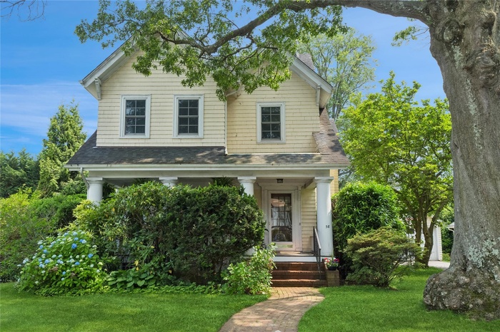 View of front of home with a front lawn, roof with shingles, and a porch