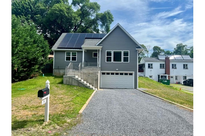 View of front of home featuring solar panels, stairs, a garage, driveway, and a front yard