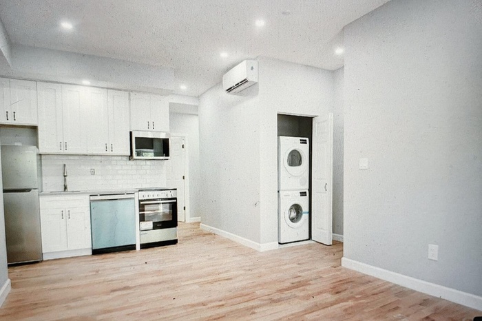 Kitchen with stacked washer / dryer, appliances with stainless steel finishes, white cabinets, light wood-style flooring, and recessed lighting