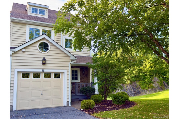 Traditional-style house with a shingled roof, covered porch, a front yard, a garage, and asphalt driveway