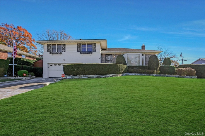 Tri-level home with an attached garage, a front yard, driveway, and a chimney
