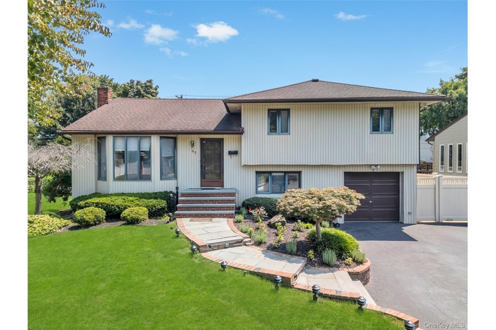 Tri-level home with asphalt driveway, a garage, a chimney, and roof with shingles