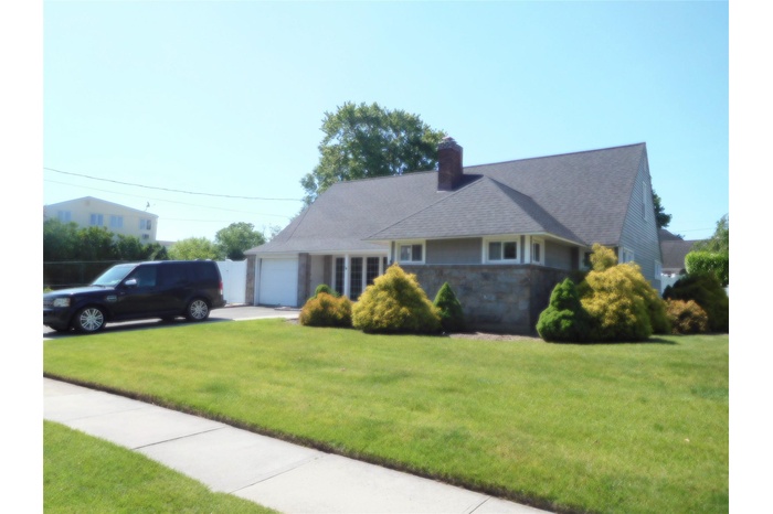 View of front of home featuring a garage, a front yard, a chimney, driveway, and stone siding