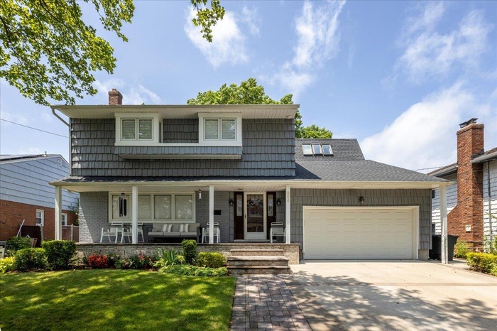 Traditional-style home with driveway, a porch, an attached garage, a front lawn, and a chimney