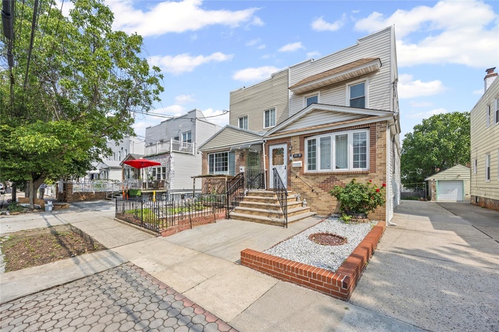 Multi unit property with an outdoor structure, brick siding, driveway, a detached garage, and a residential view