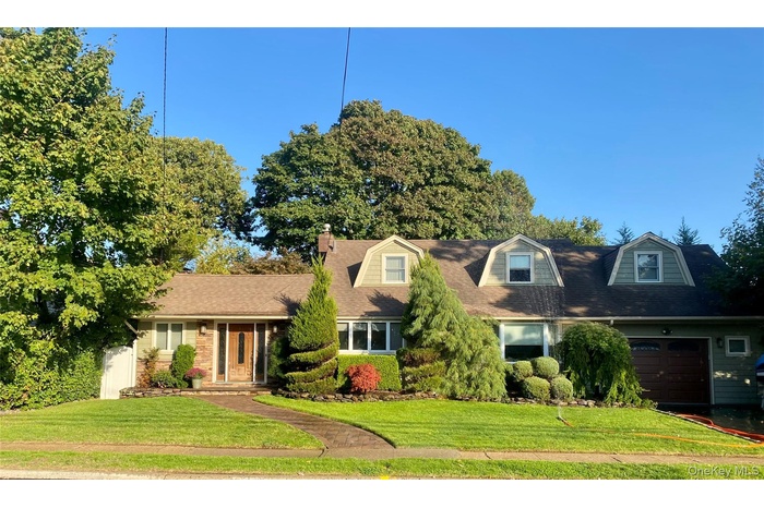 Cape cod house with a front yard, a garage, a chimney, and a shingled roof