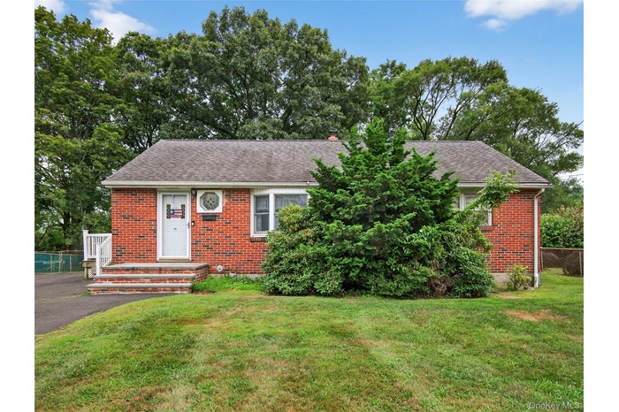 View of front of property featuring brick siding, a shingled roof, a front lawn, and a chimney