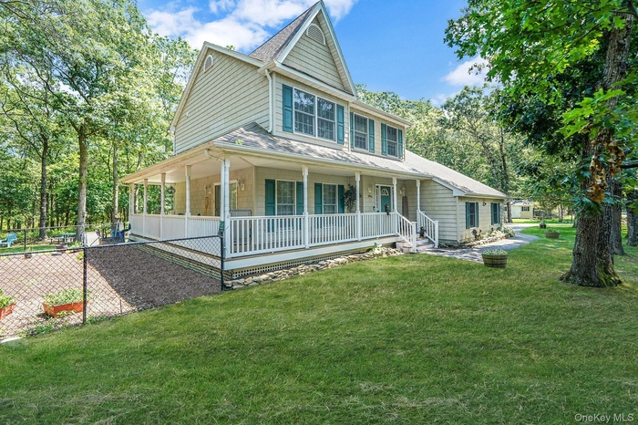 Farmhouse-style home with a front lawn, view of scattered trees, a porch, and a shingled roof