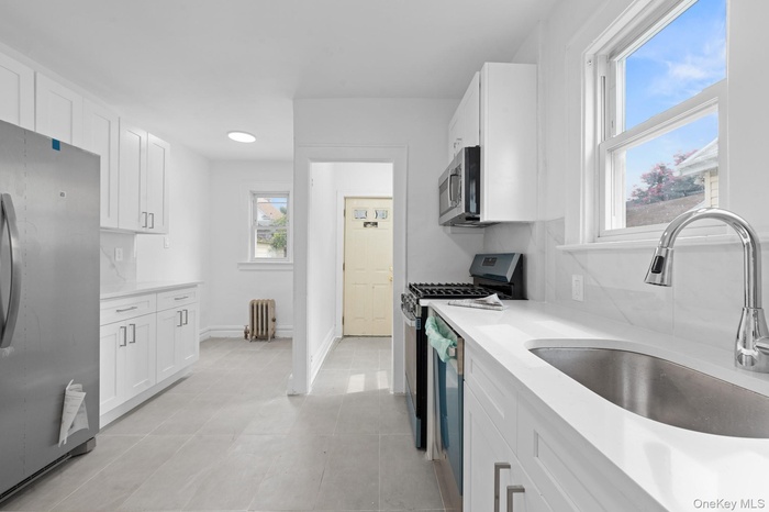Kitchen featuring stainless steel appliances, white cabinetry, light countertops, and radiator heating unit