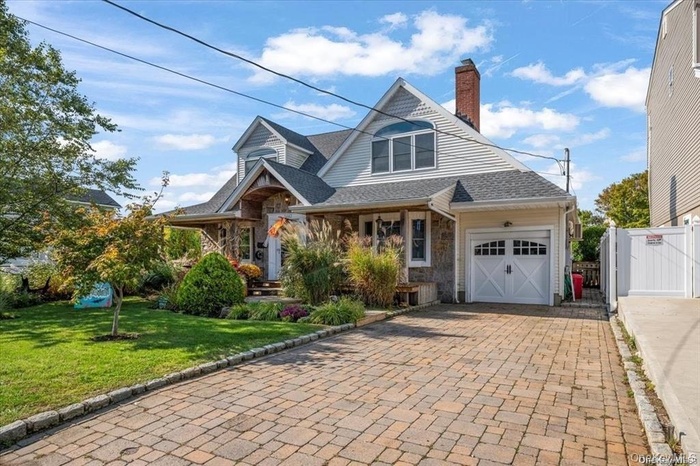 View of front of house with decorative driveway, a garage, stone siding, a chimney, and a gate