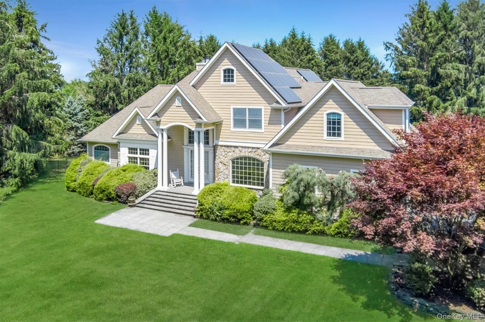 View of front of property featuring roof mounted solar panels, a front lawn, stone siding, and a chimney