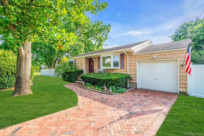 Ranch-style home with an attached garage, a shingled roof, and decorative driveway