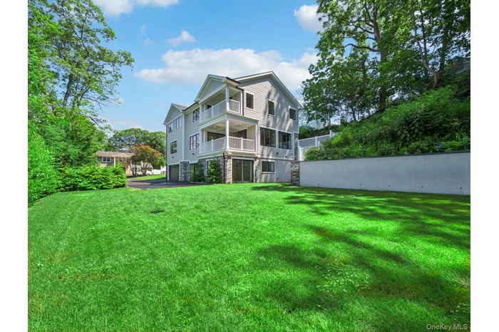 Rear view of property with an attached garage, a balcony, a lawn, stone siding, and asphalt driveway