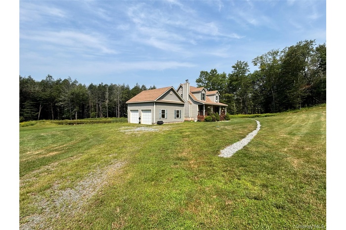 Rear view of property with driveway, a yard, a forest view, a chimney, and a garage