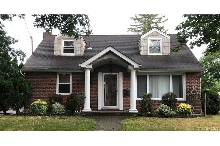 New england style home featuring a front yard, brick siding, and roof with shingles