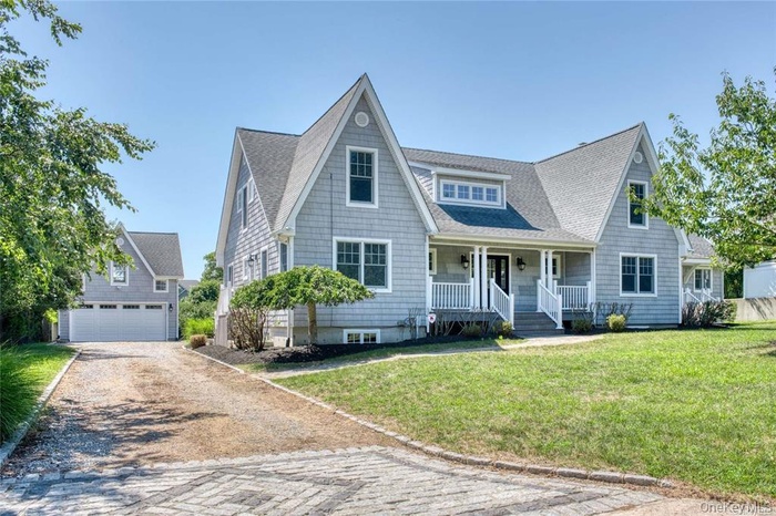 View of front of property with covered porch, a garage, an outdoor structure, a front lawn, and gravel driveway