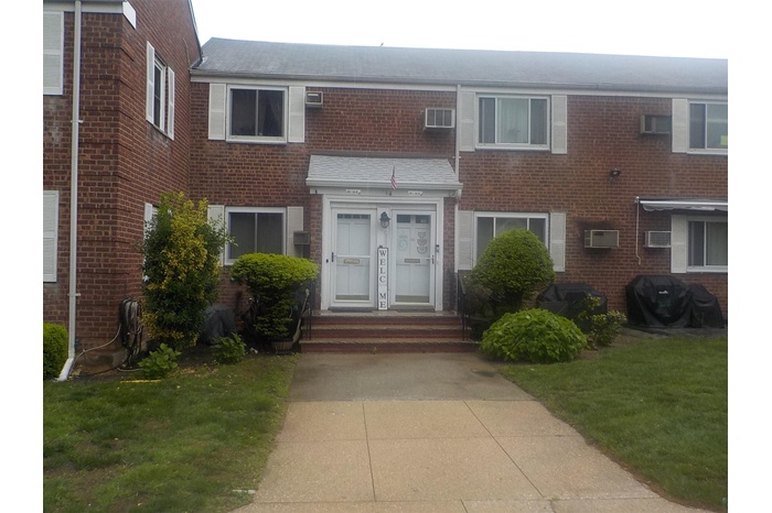 Multi unit property featuring brick siding, an AC wall unit, and roof with shingles