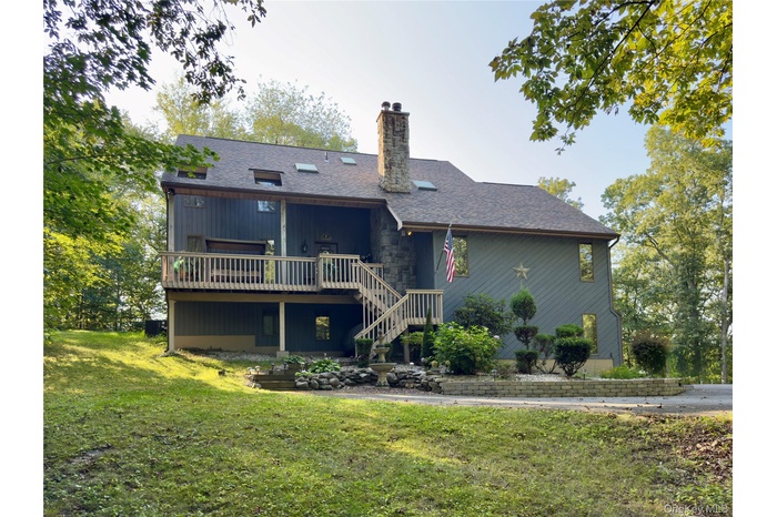 Back of house featuring a wooden deck, a chimney, stairs, a lawn, and a shingled roof