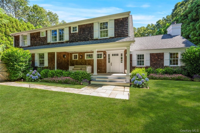 View of front of home featuring a porch, a front yard, outdoor lounge area, a chimney, and roof with shingles