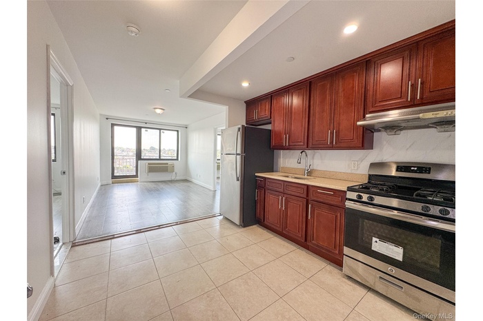 Kitchen featuring appliances with stainless steel finishes, under cabinet range hood, light tile patterned flooring, open floor plan, and dark brown c