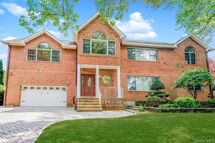 Traditional home with brick siding, a front yard, decorative driveway, and a garage