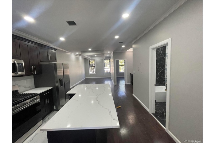 Kitchen featuring stainless steel appliances, crown molding, a kitchen island, dark wood finished floors, and light stone countertops