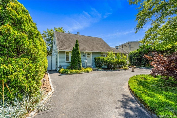 Cape cod house featuring asphalt driveway, a gate, and a shingled roof